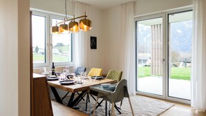 Ein Essbereich mit Holztisch, Stühlen und Blick ins Freie durch große Fenster.