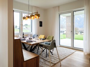 Ein Essbereich mit Holztisch, Stühlen und Blick ins Freie durch große Fenster.