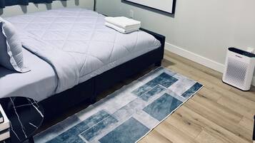 A neatly made bed with a white comforter and pillows, a blue and white patterned rug, a framed sign on the wall, and a small potted plant.