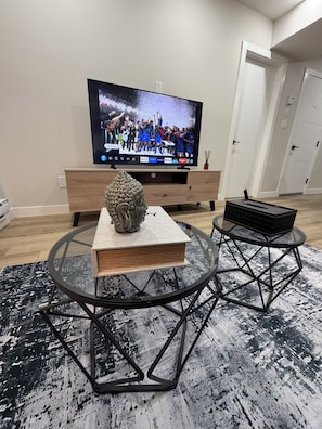 A modern living room with a flat-screen TV, a decorative bust, a book, and a coffee table. - The Onyx Suite: Minimalist Luxury w/ Gym & Parking (Regina)