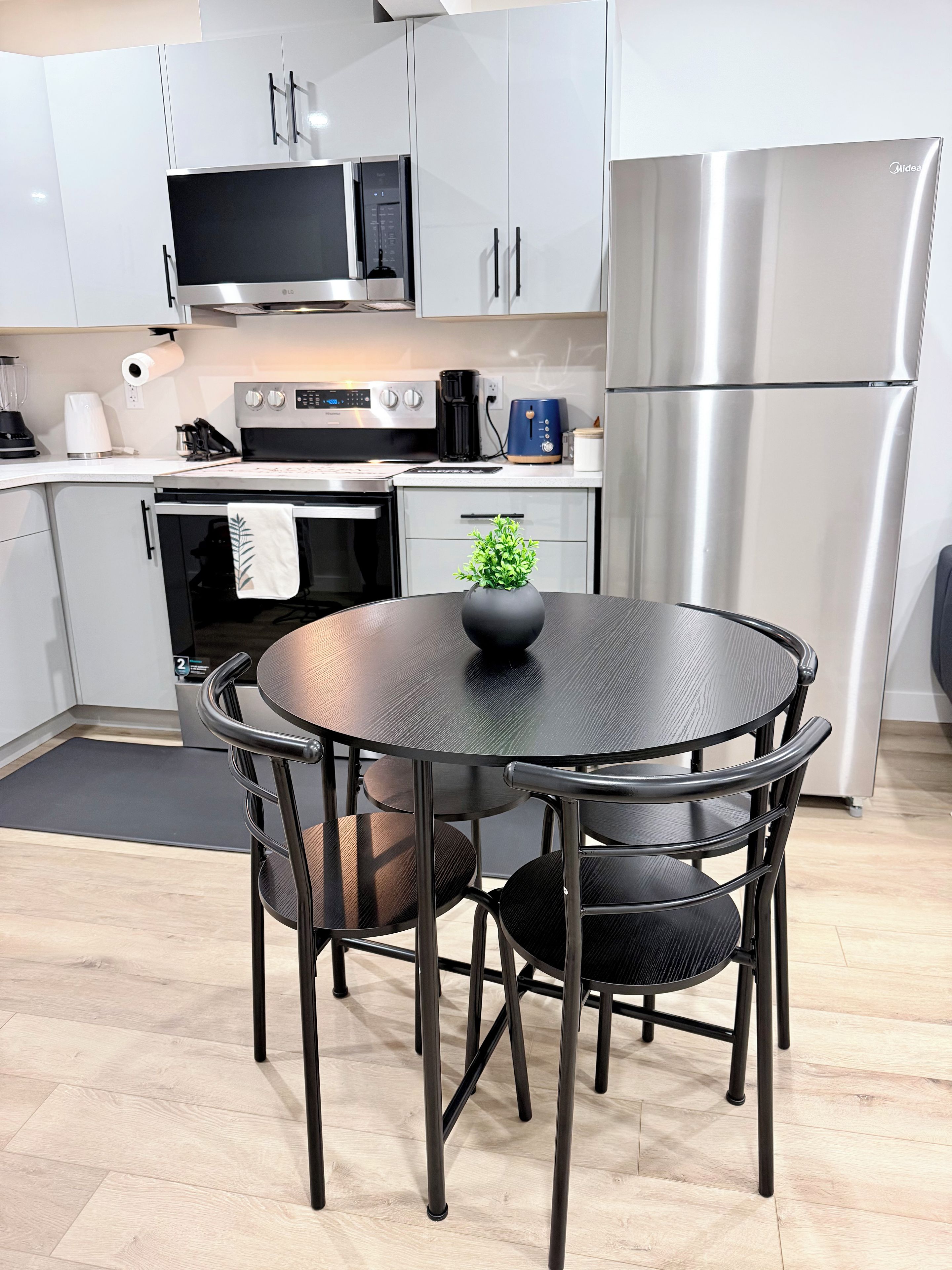 Una cocina moderna con electrodomésticos de acero inoxidable, una mesa redonda con sillas y una pequeña planta en maceta.