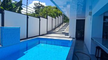 A modern indoor swimming pool with clear blue water, surrounded by white walls and a glass ceiling.