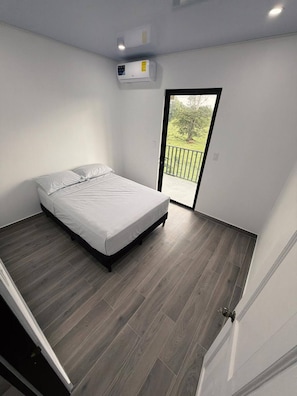 Un dormitorio con cama, puerta corrediza a un balcón y equipo de aire acondicionado.