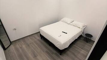 Un dormitorio pequeño y moderno con una cama, una mesita y un espejo.