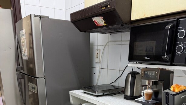 A compact kitchen with a stainless steel refrigerator, a microwave, a coffee machine, and a washing machine.