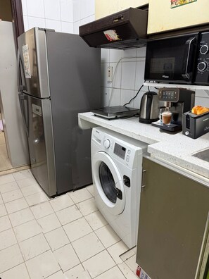 Eine kompakte Küche mit einem Edelstahlkühlschrank, einer Mikrowelle, einer Kaffeemaschine und einer Waschmaschine.