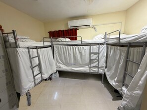 Ein Schlafsaalzimmer mit Etagenbetten, einer Klimaanlage, einem roten Vorhang und einem Metallschrank.