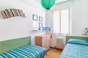 A bedroom with two beds, a bookshelf, a radiator, and a window.