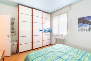 A bedroom with a bed, a wardrobe, a radiator, and a window with a cityscape view.