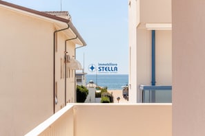 Eine enge Straße mit Häusern an beiden Seiten, freie Sicht auf das Meer und ein Schild für 'immobiliare STELLA', welches Immobilienleistungen anzeigt.