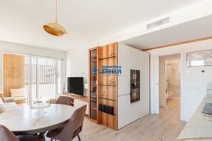 Eine moderne Küche mit Holzschränken, ein Essbereich mit Marmortisch und Blick ins angrenzende Badezimmer.