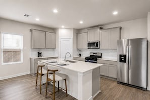 Eine moderne Küche mit einer zentralen Kochinsel, Edelstahlgeräten und hellen Schränken.