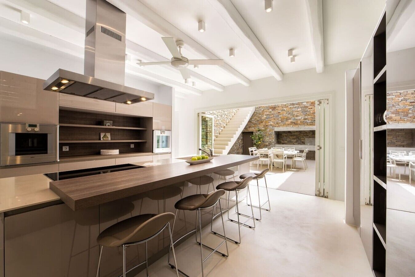 A modern kitchen with a central island, bar stools, and a stone fireplace in the dining area.