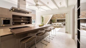 Una cocina moderna con una isla central, taburetes de bar y una chimenea de piedra en el comedor.