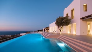 Una piscina moderna con escalones que conducen a un edificio, un árbol y vistas al mar.