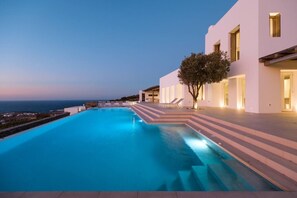 Ein moderner Pool mit Stufen, die zu einem Gebäude, einem Baum und Meerblick führen.
