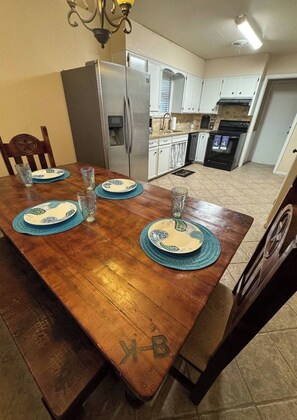 Una mesa de comedor con individuales, un refrigerador, una estufa y un lavaplatos en una cocina.