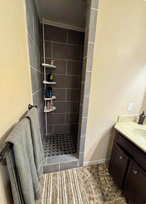 Un baño con ducha, toallero, lavamanos y piso estampado.
