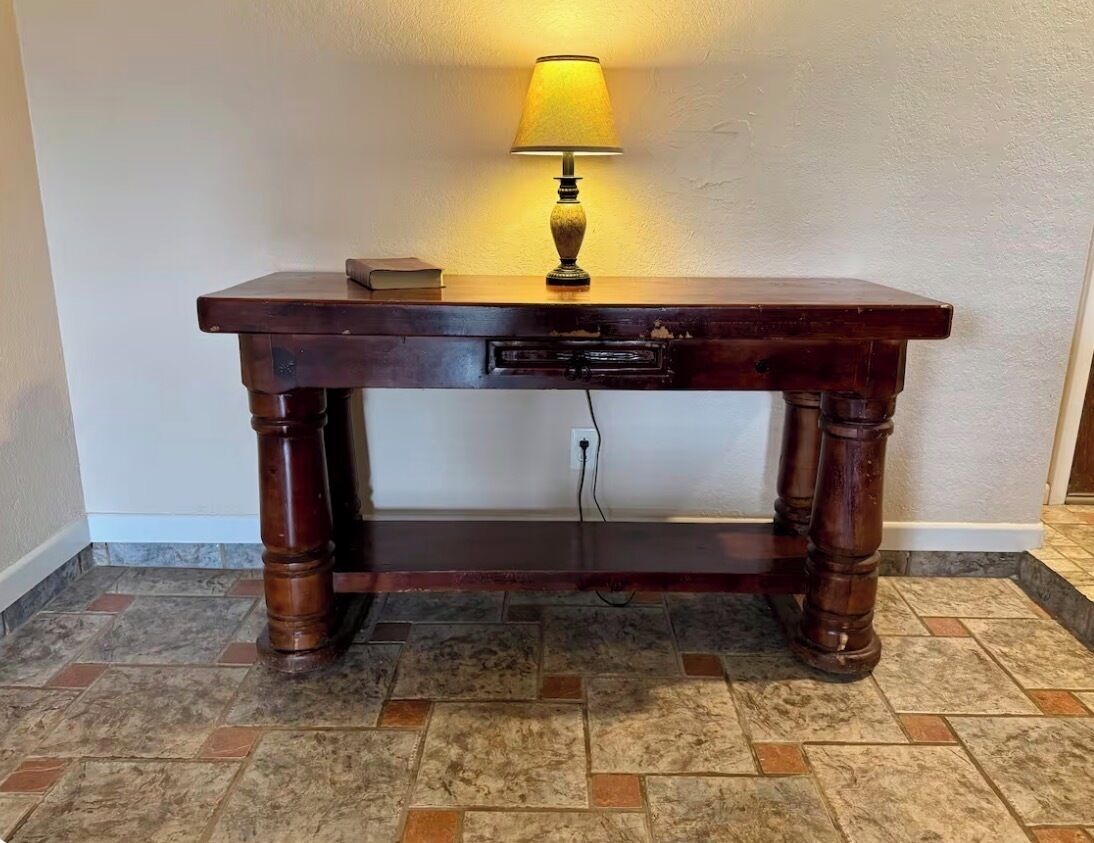 A wooden desk with a lamp, a book, and a power outlet.