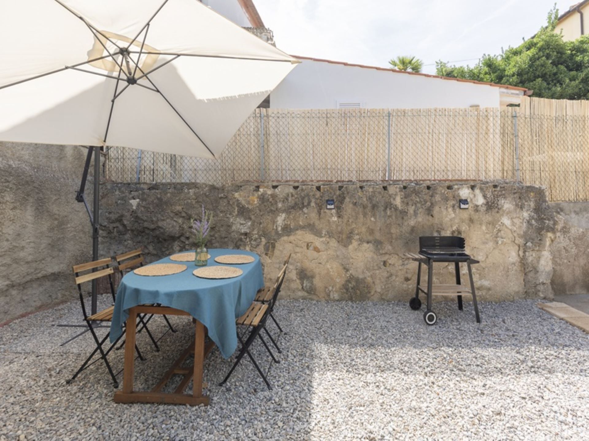 An outdoor patio with a table set for four, a grill, and a large umbrella.
