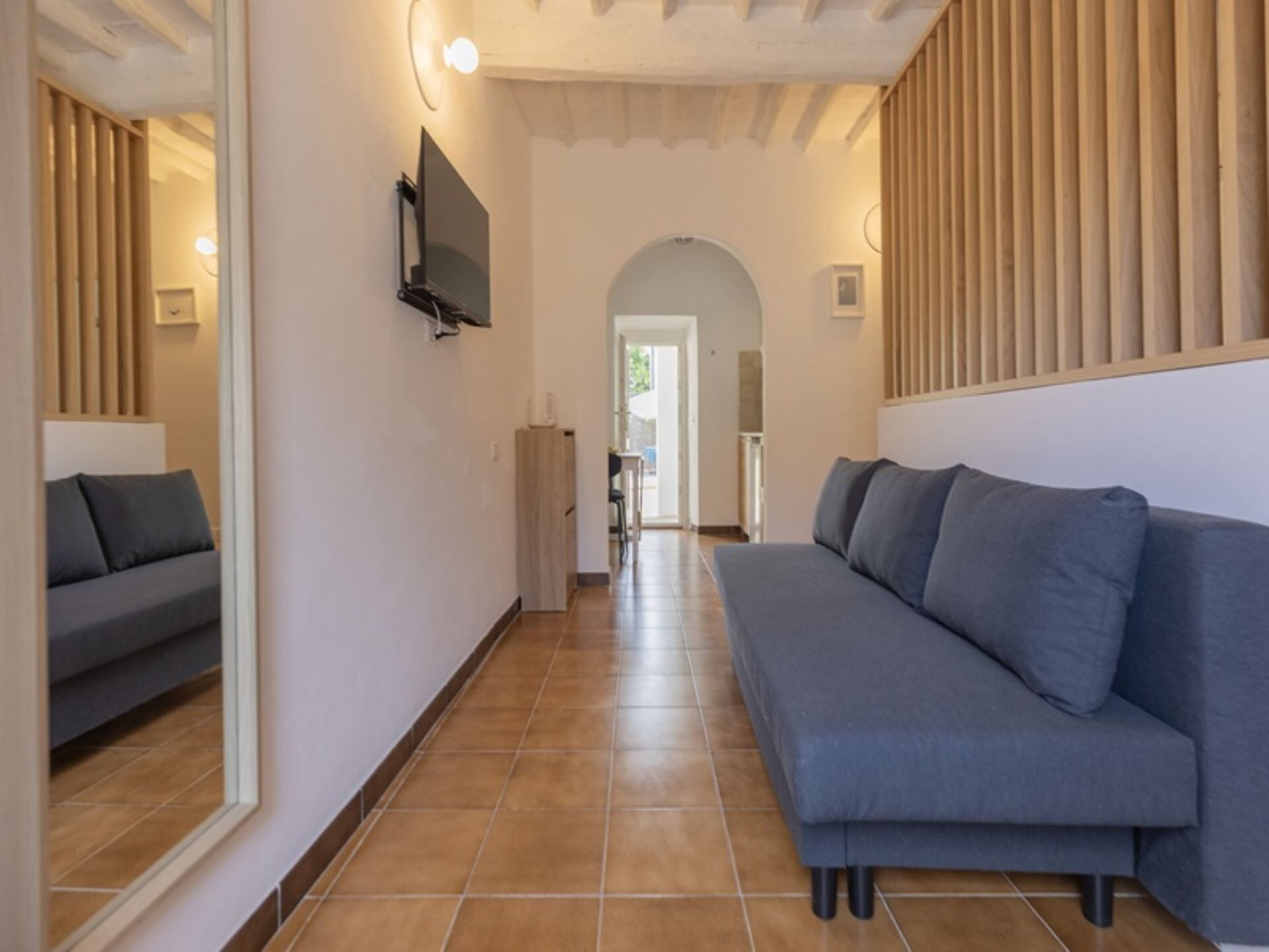 A hallway with a grey sofa, a television mounted on the wall, and a wooden slat design on the right wall.