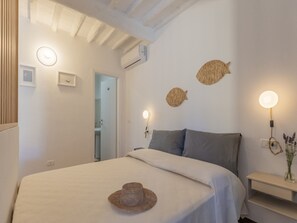 Ein Schlafzimmer mit einem Bett, Nachttischlampen, einer Wand-Klimaanlage und einer Tür zu einem weiteren Raum.