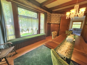 A room with large windows, a long wooden table, a green upholstered bench, and a chandelier.
