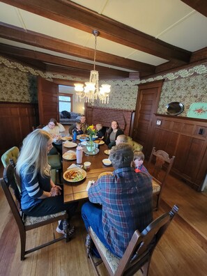 Une salle à manger familiale avec une table en bois, des chaises, un lustre et une cheminée.