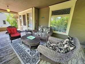 Une véranda couverte avec des meubles en osier, un fauteuil rouge rembourré et un tapis à motifs.