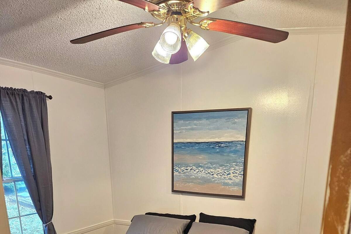 A bedroom with a bed, a ceiling fan, a painting, and a small table.