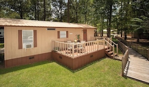 A single-story wooden cabin with a fenced deck, a small outdoor seating area, and a staircase leading to a deck. - Sunburst RV Resort (Milton)