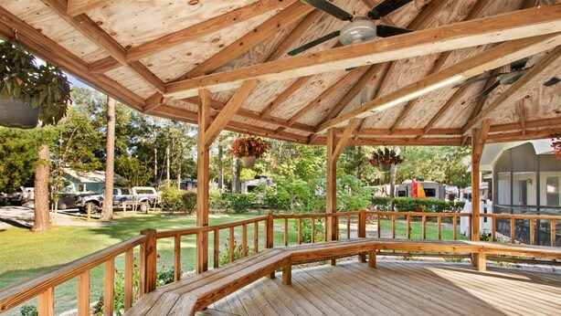 A wooden deck with a railing, a ceiling fan, and hanging flower baskets. - Sunburst RV Resort (Milton)