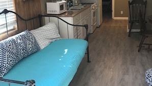 A compact living space with a kitchenette, a bed with patterned pillows, and a dining area with a chair. - Sunburst RV Resort (Milton)