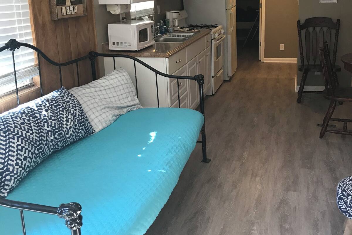 A compact living space with a kitchenette, a bed with patterned pillows, and a dining area with a chair.