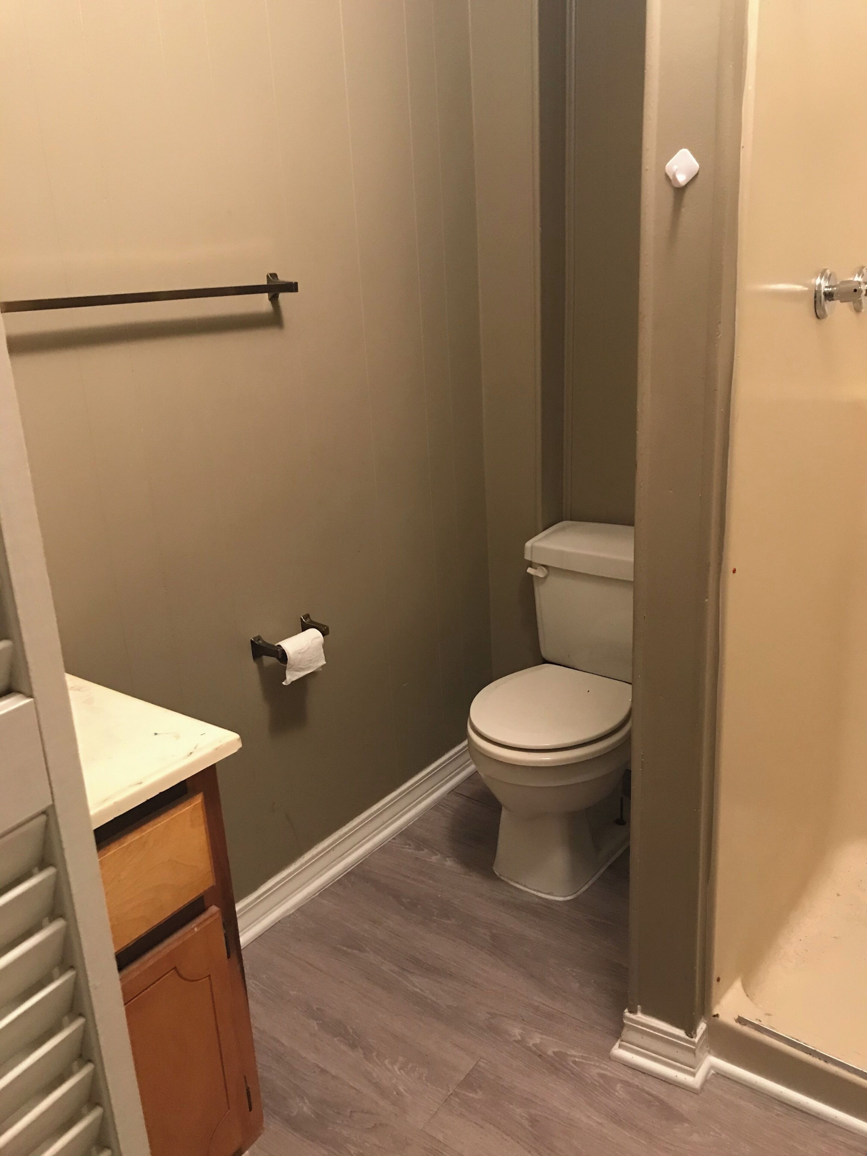 A bathroom with a toilet, a towel rack, and a wooden cabinet.