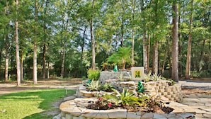 A stone fire pit surrounded by plants and a small stone house with a frog logo. - Sunburst RV Resort (Milton)
