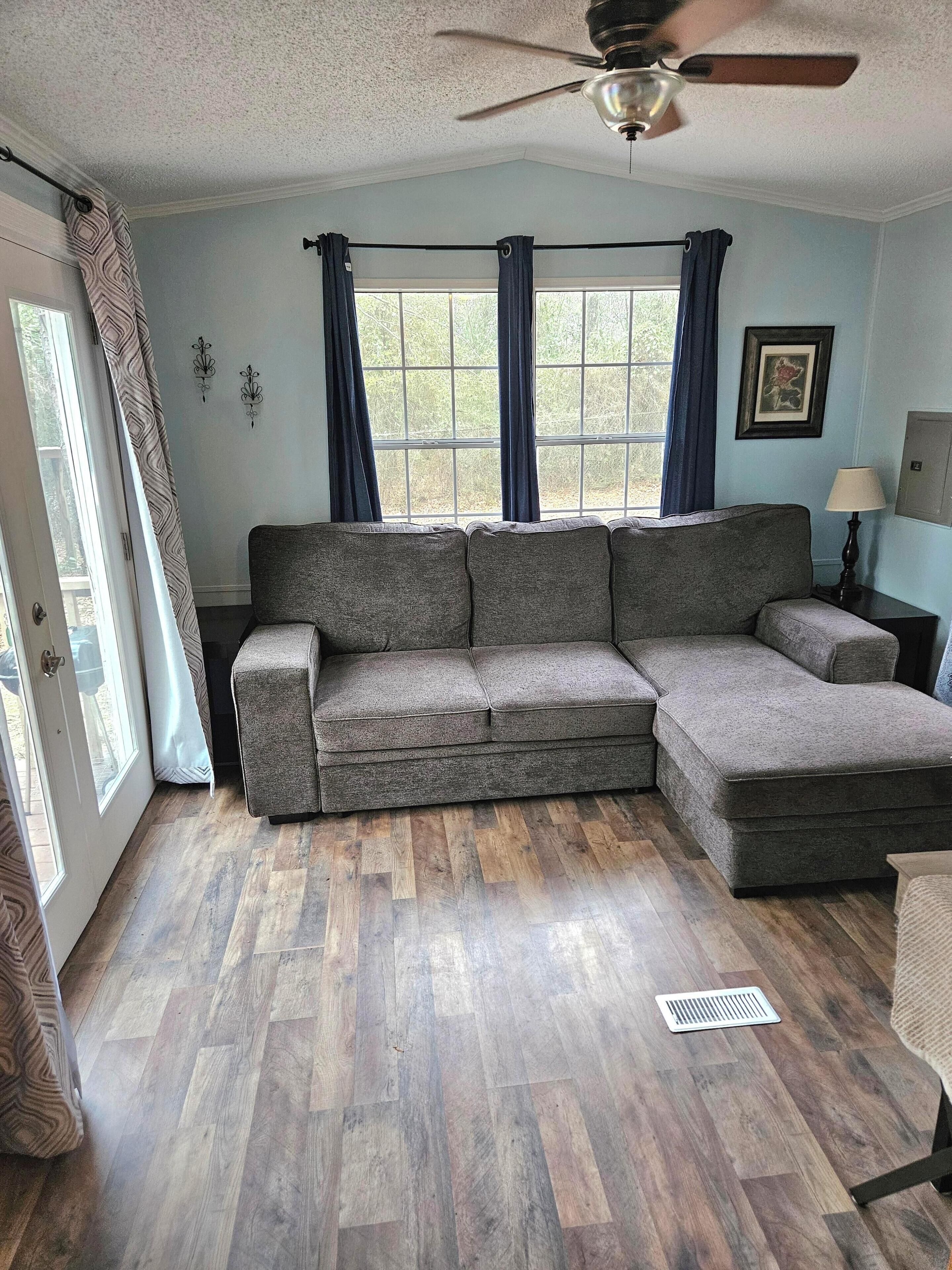 A living room with a sectional sofa, a ceiling fan, a window with curtains, and a door leading outside.