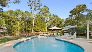 A swimming pool with lounge chairs and umbrellas, surrounded by trees and a fenced area. - Sunburst RV Resort (Milton)