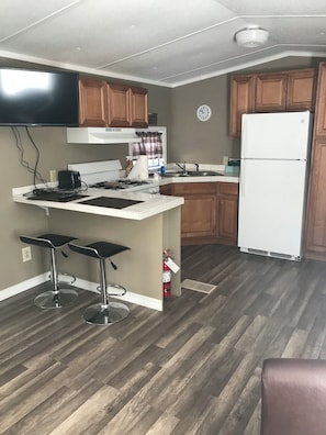 A kitchen with a white refrigerator, wooden cabinets, a black stove, and two bar stools.