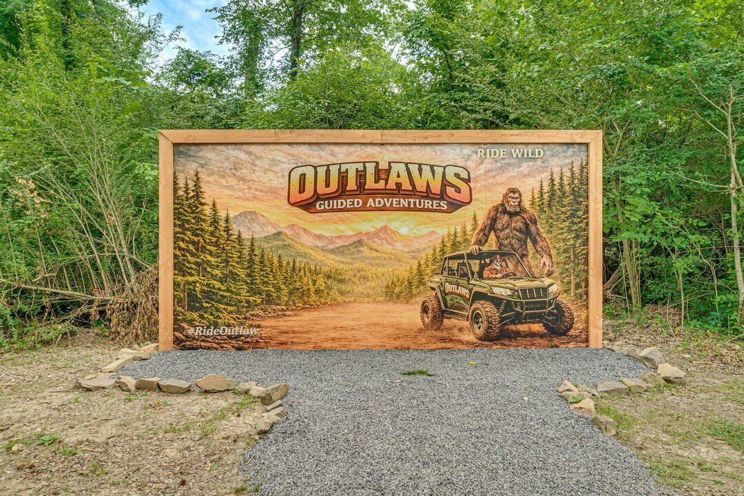 Um mural emoldurado com uma paisagem acidentada ao ar livre, uma figura imponente e um veículo com a inscrição 'OUTLAWS GUIDED ADVENTURES'.
