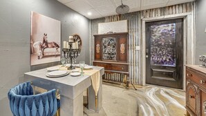 Een eetruimte met een tafel voor vier personen, een blauwe bekleden stoel, een decor kast en een deur met een geëtst glaspaneel.