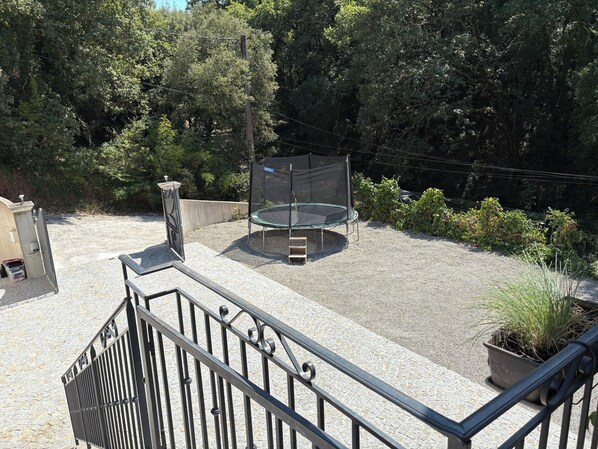 A covered trampoline in a gravel area with surrounding greenery and a metal railing. - VILLA AU CALME (Vidauban)