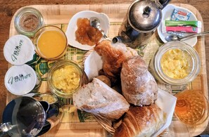 Una mesa de madera con diversos alimentos y condimentos, incluyendo pan, mantequilla, mermelada y una tetera.