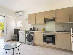 Een compacte keuken met een wasmachine, vaatwasser, oven en een klein eethoekje met een glazen tafel.