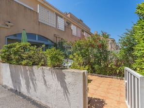 A building with a concrete entrance, a tiled patio, and a variety of plants and shrubs. - Les Marines du Levant by Interhome (Hyères)