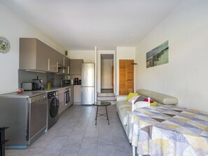 A compact kitchen with modern appliances, a dining area with a table and sofa, and a door leading to a hallway. - Les Marines du Levant by Interhome (Hyères)