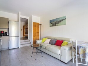 A compact living space with a kitchenette, a sofa with colorful cushions, a small round table, and a painting on the wall. - Les Marines du Levant by Interhome (Hyères)