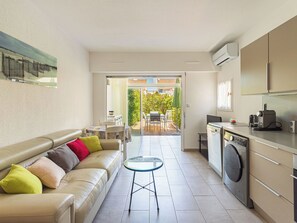 A compact living space with a sofa, a small table, a washing machine, and a kitchenette. - Les Marines du Levant by Interhome (Hyères)