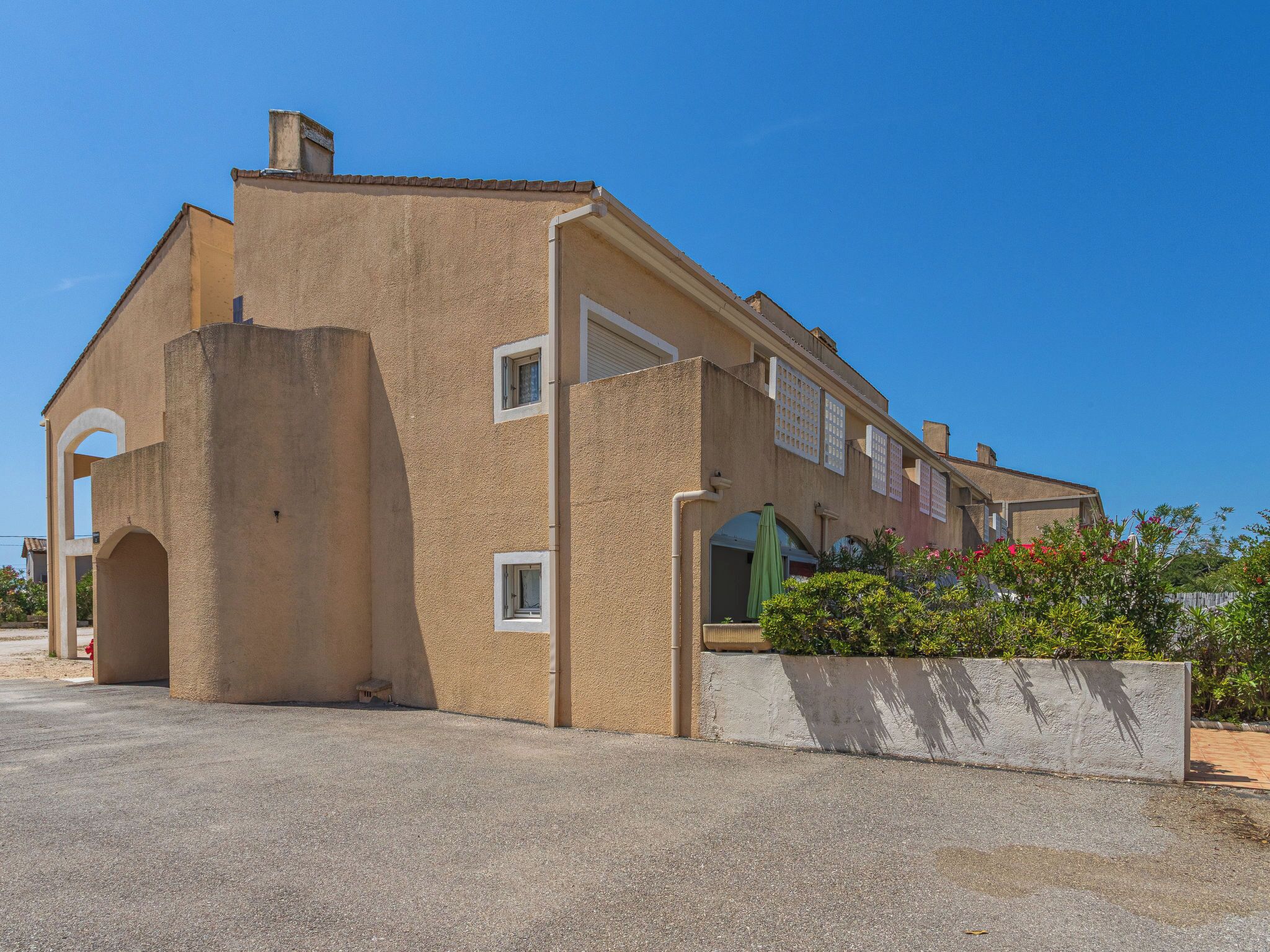 Een gebouw met twee verdiepingen, een plat dak, een balkon en een kleine tuin.