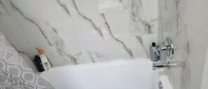 A bathroom with a white bathtub, marble walls, and a shower area. - New Cozy One bed Suite  close to downtown Edmonton.For Leisure and Business Stay (Northwest)